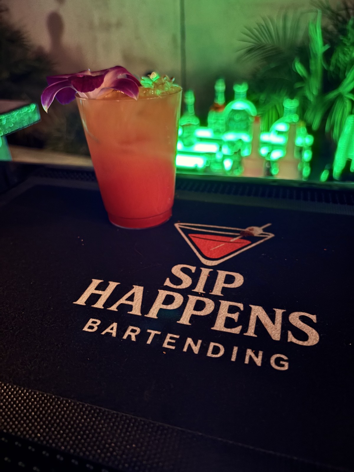 Signature cocktail garnished with a purple orchid on the Sip Happens Bartending bar mat