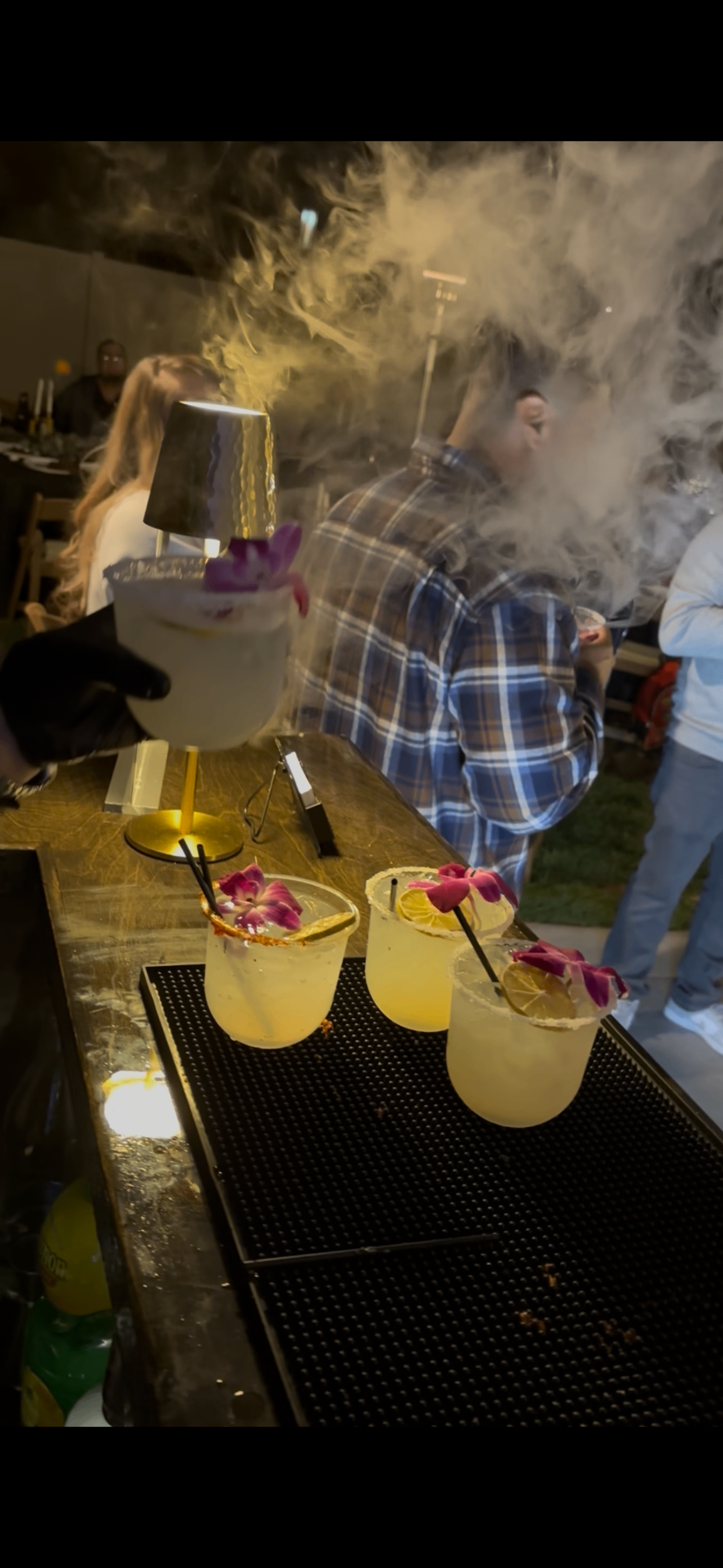 Orchid-garnished cocktails on the bar under a smoky haze at night